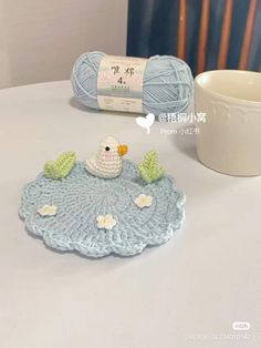 a crocheted bird sits on top of a doily next to a ball of yarn