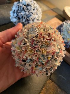 a hand holding a ball made out of small pieces of paper and other things in the background