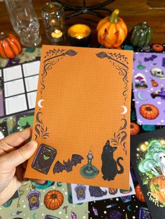 a person holding up an orange halloween card with black cats and witches on it, surrounded by other cards