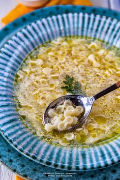 a spoon full of soup on top of a blue and white plate with green trim