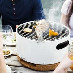 people sitting around a table with food and drinks on it, while one person is grilling fish