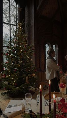 a woman standing in front of a christmas tree with candles on the table next to it