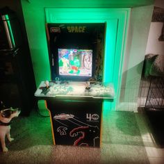 a small dog standing in front of a video game machine that is lit up with green light