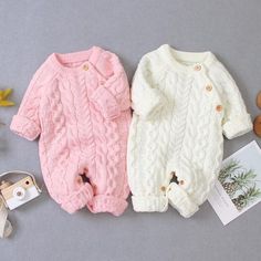 two baby sweaters sitting next to each other on top of a gray surface with autumn leaves