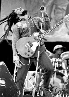 a black and white photo of a man with dreadlocks on his head playing an electric guitar