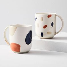 two coffee mugs sitting next to each other on top of a white countertop