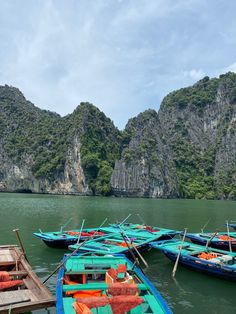 there are many small boats that are docked in the water near some mountains and rocks