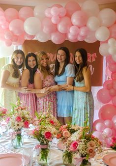 a group of women standing next to each other in front of a table with pink and white balloons