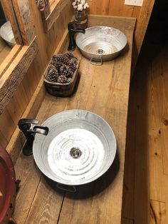 two metal bowls sitting on top of a wooden table next to each other with pine cones in them