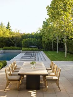 an outdoor dining table and chairs in front of a swimming pool with trees on the other side