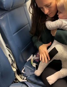 a woman holding a child in her arms while sitting on a blue seat next to another person