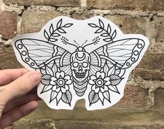 a hand holding up a sticker with a skull and butterfly design on the back