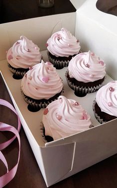 cupcakes with pink frosting in a white box next to a pink ribbon