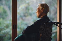 an older woman sitting in a chair looking out the window