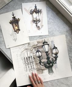 a person is holding up some drawings on a table next to a lamp and window