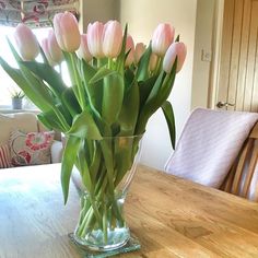 a vase filled with pink tulips sitting on top of a wooden dining room table