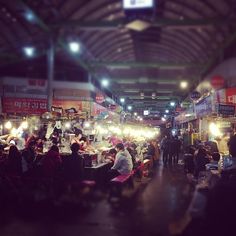 people are sitting at tables in an indoor market area with lights on and signs hanging from the ceiling