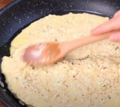 a wooden spoon mixing food in a black skillet on a wood counter top, with rice and parmesan sprinkles