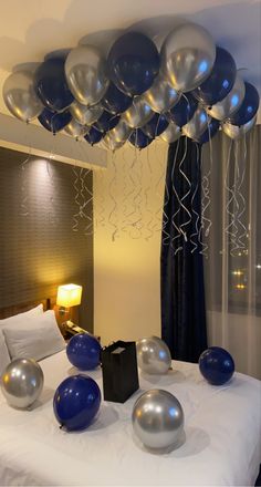 blue and silver balloons floating from the ceiling above a bed