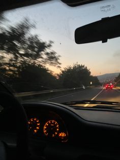 the dashboard of a car driving down a road at dusk with trees and mountains in the background