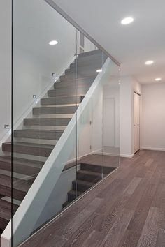 an empty room with wood floors and glass railings on the stairs leading up to the second floor