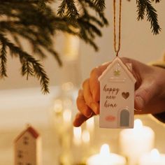 a person holding a house ornament in front of a christmas tree with candles