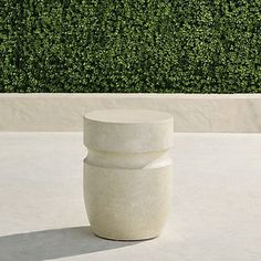 a large white vase sitting on top of a cement floor next to a green hedge