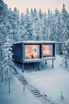 a small cabin in the middle of a snowy forest with stairs leading up to it