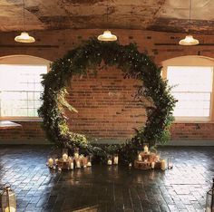 a large circular wreath is surrounded by candles and greenery in the middle of an empty room