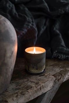 a lit candle sitting on top of a wooden table next to a vase and blanket