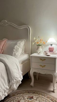 a white bed sitting next to a night stand on top of a rug in a bedroom