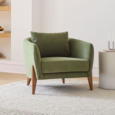 a green chair sitting on top of a rug next to a white vase with candles in it