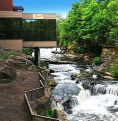 a river running through a lush green forest next to a tall building with a sign on it