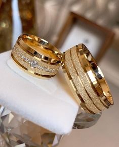 two gold wedding rings sitting on top of a white ring box next to each other