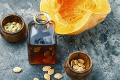 a bottle of almond oil next to two wooden bowls filled with nuts and pumpkin seeds