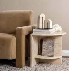 a chair and table with books on it in front of a beige wall, next to a white flower