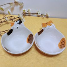 two white bowls with cats on them sitting next to each other