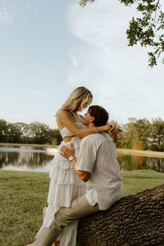 a man and woman sitting on top of a tree in front of a body of water