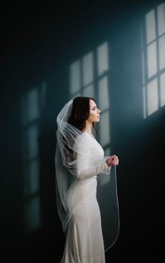 a woman in a white dress and veil standing by a window with sunlight streaming through the windows