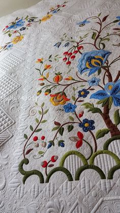 an embroidered quilt with flowers and leaves on the bottom is laying on top of a bed