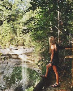 a woman sitting on a log in front of a waterfall and looking at the water