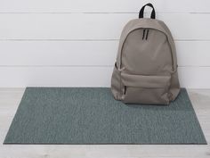 a gray backpack sitting on top of a rug next to a white wall and wooden floor