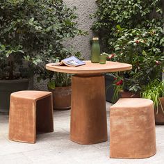 an outdoor table with three stools in front of plants and potted planters