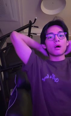 a young man wearing glasses sitting in front of a computer desk with his hands on his head