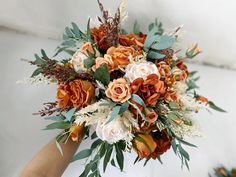 a bridal bouquet with orange, white and green flowers is held by someone's hand