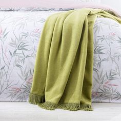 a green blanket sitting on top of a bed next to a white wall with pink flowers