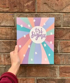 a person holding up a canvas with the words tri stigma on it in front of a brick wall