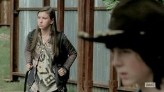 two young women standing next to each other in front of a metal fence and building