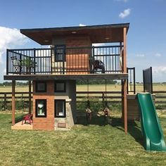 a small house with a green slide in front of it and a wooden deck on the top floor