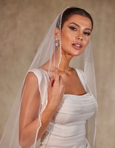 a woman in a white wedding dress with a veil over her head and pearls on the side